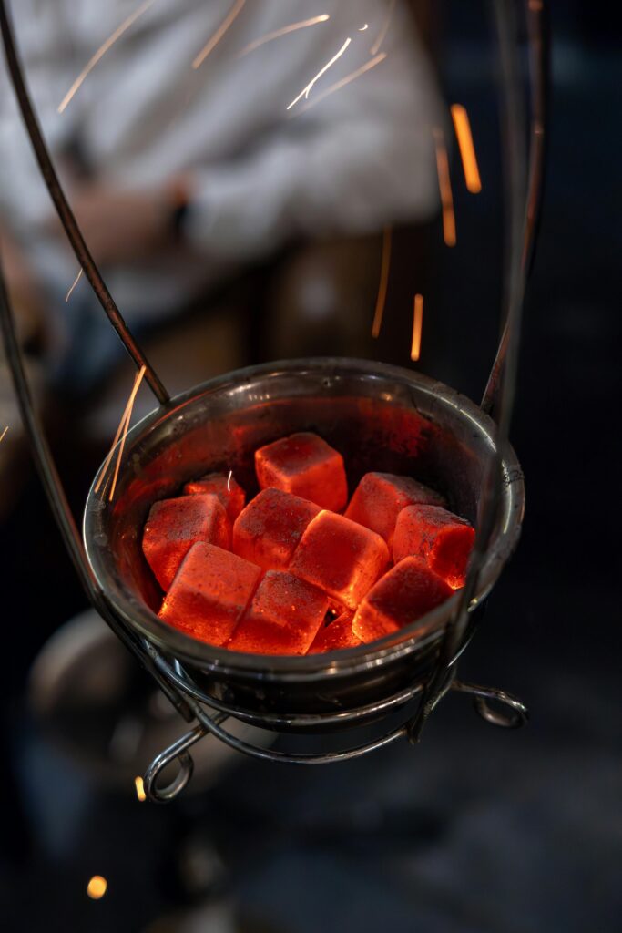 Close-up of red hot charcoal cubes emitting sparks in a metal holder.